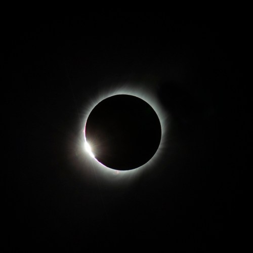 A solar eclipse with a darkened sun surrounded by a glowing halo of light against a black sky.