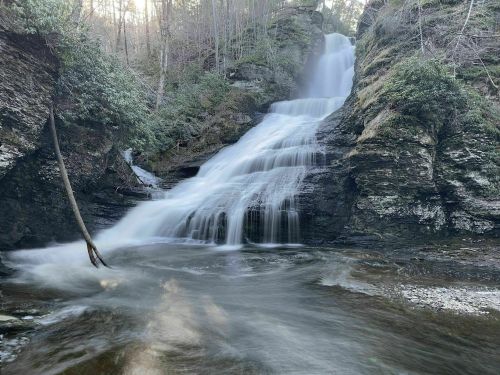 A serene waterfall cascading over rocky cliffs, surrounded by lush greenery and a tranquil stream below.