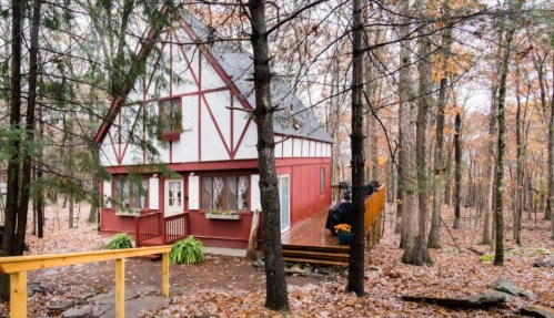 A red and white house nestled among trees in a forest, surrounded by fallen leaves in autumn.
