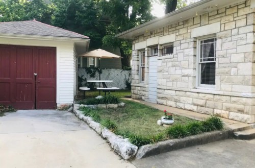 A stone house with a small garden, a picnic table, and a garage in a shaded outdoor area.