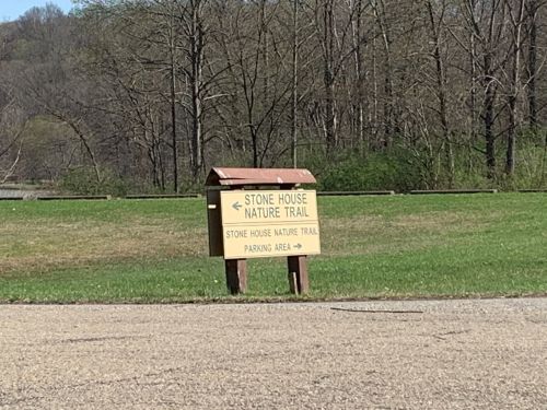 Sign for Stone House Nature Trail with directions to the trail and parking area, set against a wooded background.