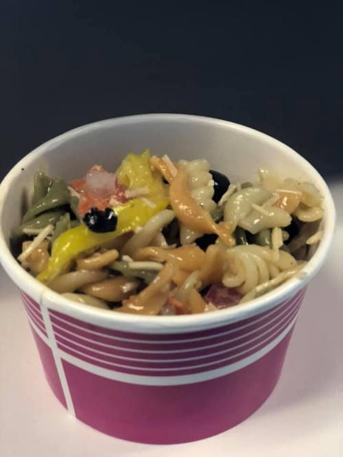 A colorful pasta salad with various vegetables served in a pink cup.