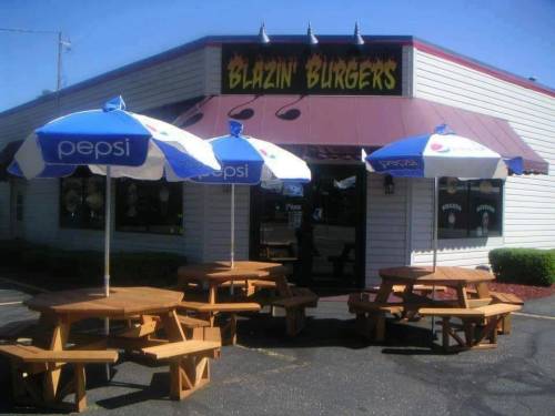 Exterior of Blazin' Burgers with picnic tables and blue umbrellas in a sunny parking lot.