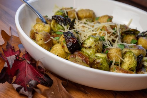 A bowl of roasted Brussels sprouts and gnocchi topped with grated cheese, surrounded by autumn leaves.