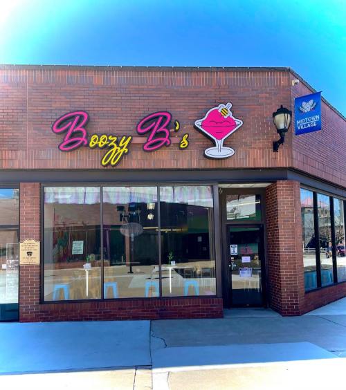 Exterior of Boozy B's, a vibrant bar with colorful signage and large windows, located in Midtown Village.