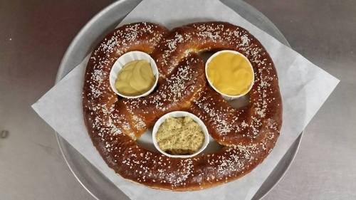 A large, soft pretzel on a tray, served with three dips: yellow mustard, spicy mustard, and a brown mustard.