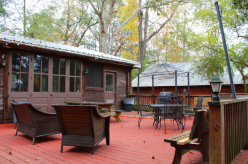 A cozy outdoor deck with seating, a gazebo, and a grill, surrounded by trees and autumn foliage.