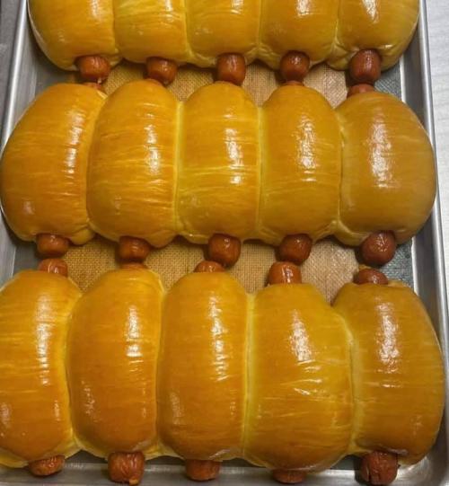 A tray of golden-brown, soft bread rolls with small sausages peeking out from between them.