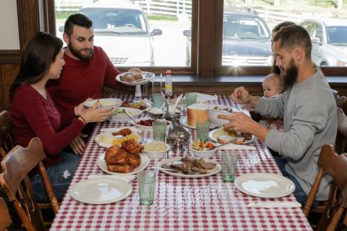 A family enjoys a hearty meal at a table filled with various dishes, including fried chicken and sides.