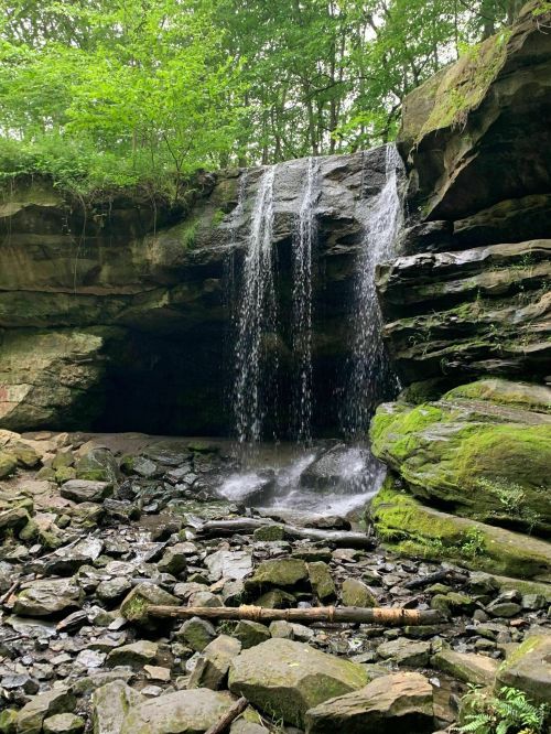 A serene waterfall cascades over rocky cliffs, surrounded by lush greenery and moss-covered stones.