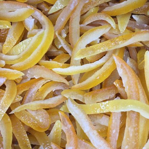 Close-up of thinly sliced, candied citrus peels in vibrant yellow and orange hues, glistening with sugar.
