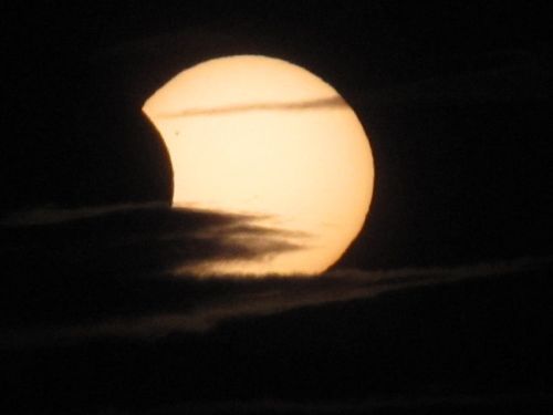 A partially eclipsed sun peeks through dark clouds, creating a striking silhouette against the sky.