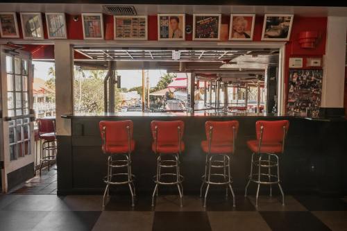 A retro diner interior featuring red bar stools and framed photos on the walls, with a view of the outside.