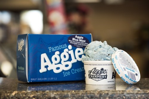 A container of Aggie Blue Mint ice cream with a scoop on a counter, featuring the Aggie Creamery logo.