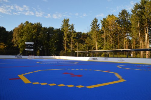 A brightly colored blue sports court with yellow and red markings, surrounded by trees and a clear sky.