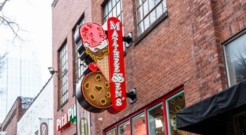 A brick storefront featuring an ice cream shop sign, with a large ice cream cone sculpture outside.