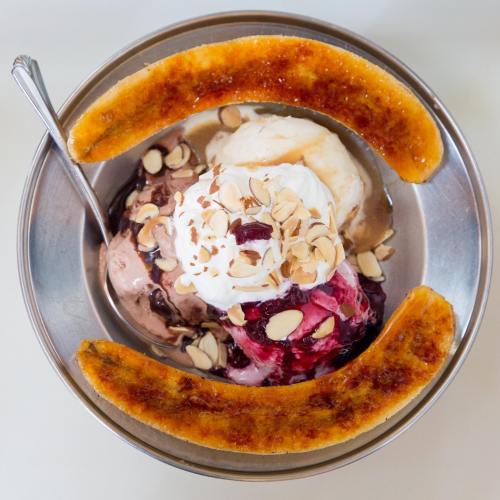 A bowl of ice cream topped with whipped cream, nuts, and two caramelized banana halves.