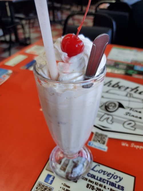 A tall glass of milkshake topped with whipped cream and a cherry, served with a straw and spoon.