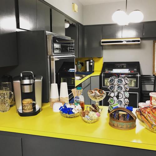 A modern kitchen with gray cabinets, yellow countertops, and a variety of snacks and drinks displayed on the counter.