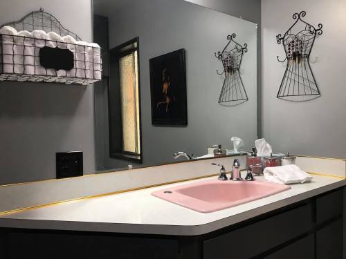 A bathroom with a pink sink, gray walls, a towel rack, and decorative wall art.