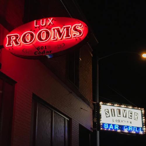 Neon signs for Lux Rooms and Silver Bar Grill illuminated at night on a city street.