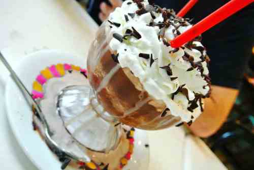 A delicious chocolate sundae topped with whipped cream, chocolate sprinkles, and two red straws in a glass dish.