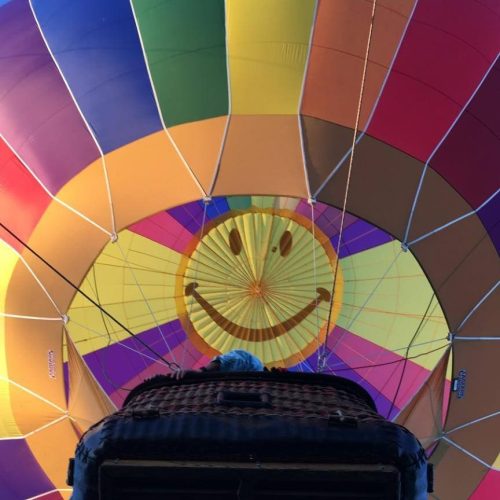 View from inside a colorful hot air balloon, featuring a large smiling face design on the canopy above.