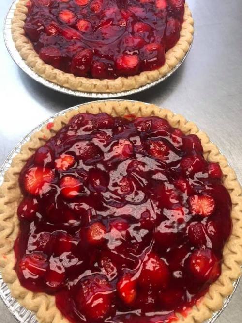 Two freshly baked strawberry pies with a glossy red glaze, resting in silver pie tins.