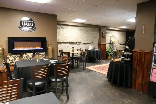 Cozy bakery and café interior with tables, a fireplace, and stone walls, creating a warm atmosphere.