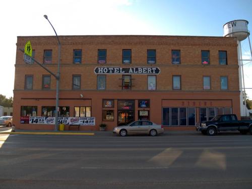 Exterior view of Hotel Albert, a brick building with neon signs, parked cars, and a nearby water tower.