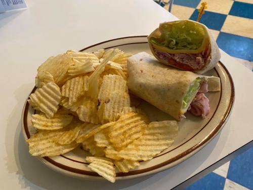A plate with a wrap filled with lettuce and turkey, accompanied by a side of ridged potato chips.