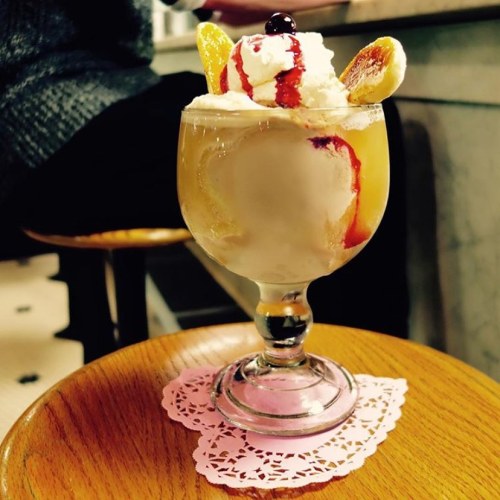 A colorful dessert sundae in a glass, topped with whipped cream, fruit, and syrup, served on a lace doily.