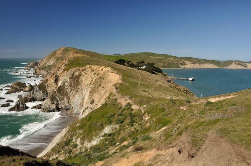 A scenic coastal view featuring cliffs, a sandy beach, and a calm blue ocean under a clear sky.