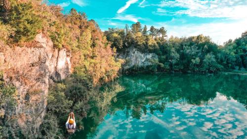 A person zip-lining over a serene, turquoise lake surrounded by lush greenery and rocky cliffs under a blue sky.