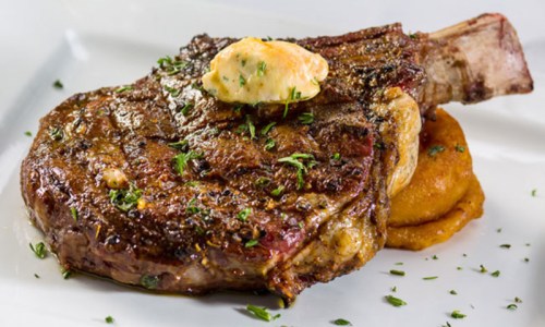 A juicy ribeye steak topped with herb butter, served on a bed of creamy mashed potatoes, garnished with herbs.