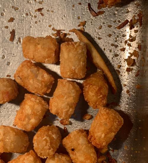 A close-up of crispy golden tater tots scattered on a metal baking sheet.