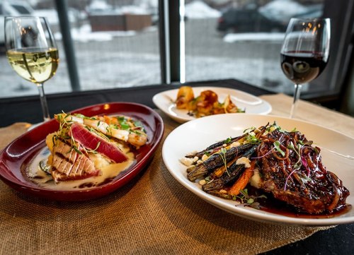 A table setting with two gourmet dishes: seared fish with sauce and a meat dish, accompanied by white and red wine glasses.