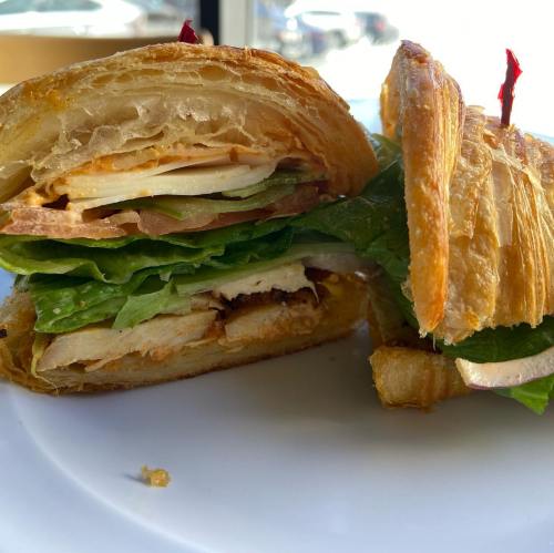 A cross-section of a flaky croissant sandwich filled with lettuce, sliced turkey, and other fresh ingredients.