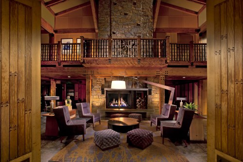 Cozy lodge interior with stone fireplace, wooden beams, and comfortable seating arranged around a central table.