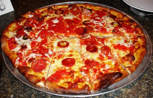 A round pizza topped with pepperoni, cheese, and tomato sauce, sliced into eight pieces on a metal tray.