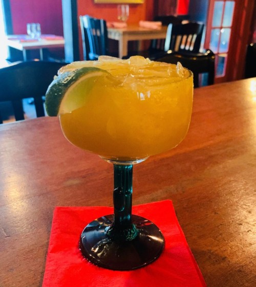 A vibrant yellow margarita with ice and a lime wedge, served in a decorative glass on a red napkin.