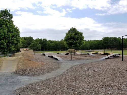 A bike park featuring wooden ramps and paths surrounded by trees and a grassy area under a cloudy sky.