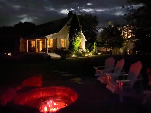 A cozy house illuminated at night, with a glowing fire pit and Adirondack chairs in the foreground.