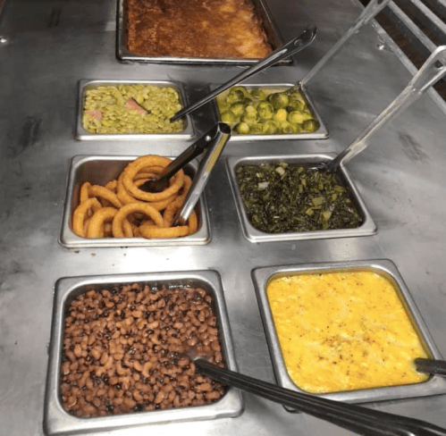 A metal serving tray with various dishes: greens, black-eyed peas, curly fries, and a cheesy casserole.