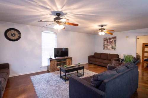 Cozy living room with two sofas, a coffee table, TV, and ceiling fans, featuring warm lighting and a decorative wall.