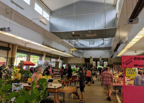 A bustling indoor market with vendors, shoppers, and colorful displays of fresh produce and flowers.