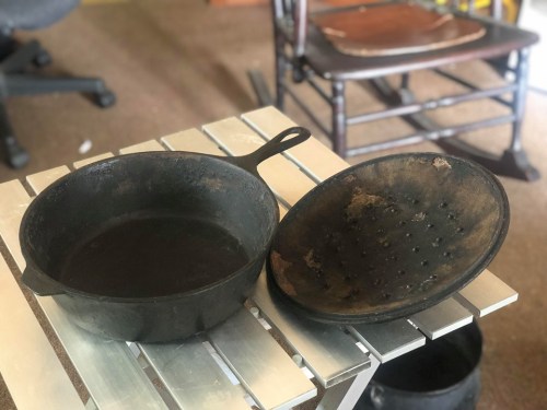 A cast iron skillet and a matching lid on a metal table, with a rustic background featuring a wooden chair.