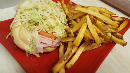 A sandwich with lettuce and tomato beside a serving of golden French fries on a red plate.