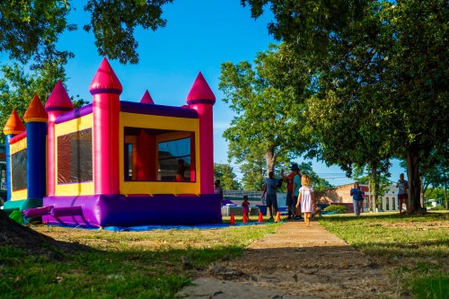 A colorful bounce house in a park with children and adults enjoying the sunny day. Trees and a clear blue sky in the background.