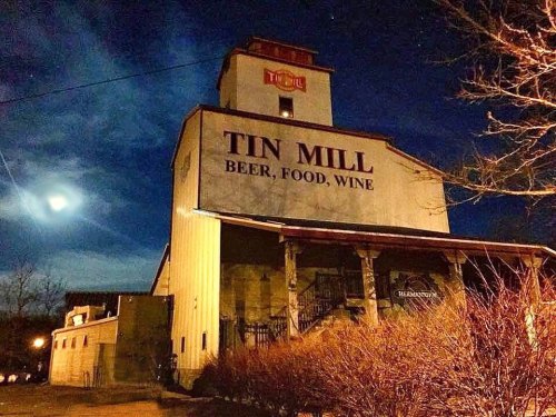 A historic building at night with a sign reading "Tin Mill Beer, Food, Wine" under a moonlit sky.